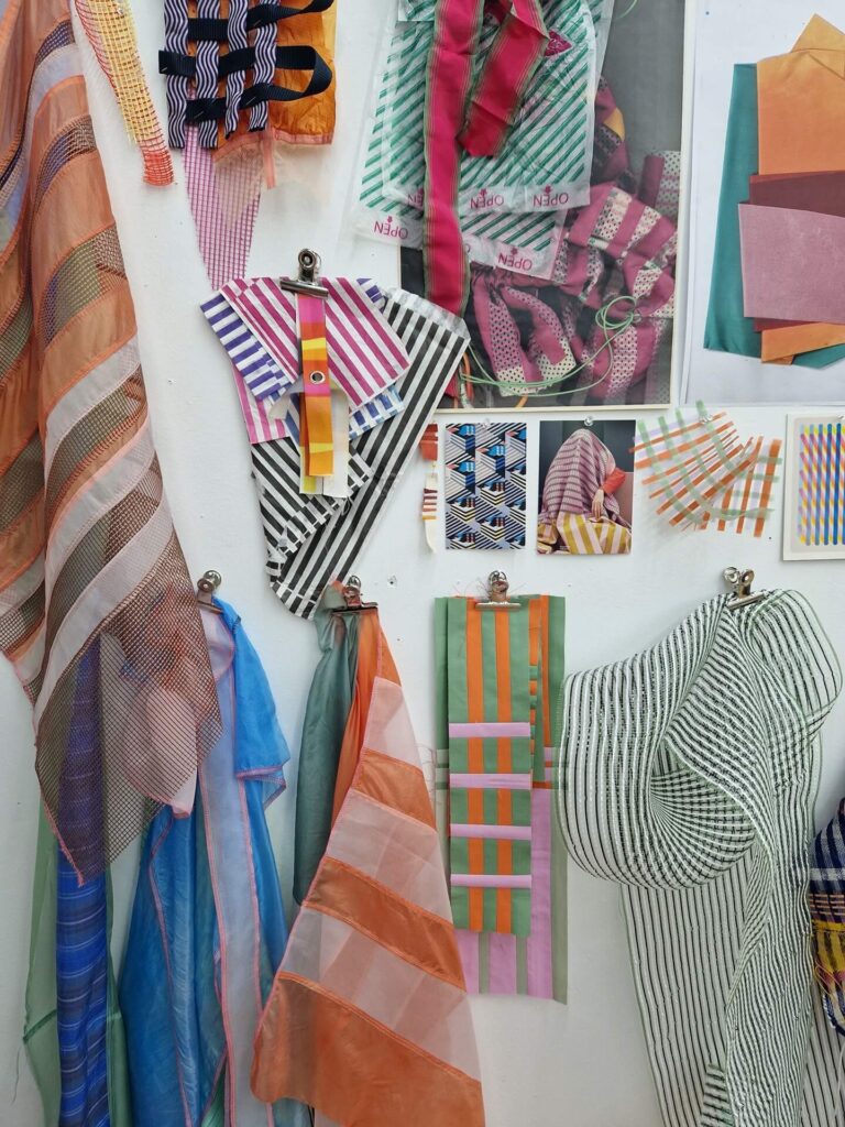 A selection of brightly coloured textile samples pinned on a white studio wall